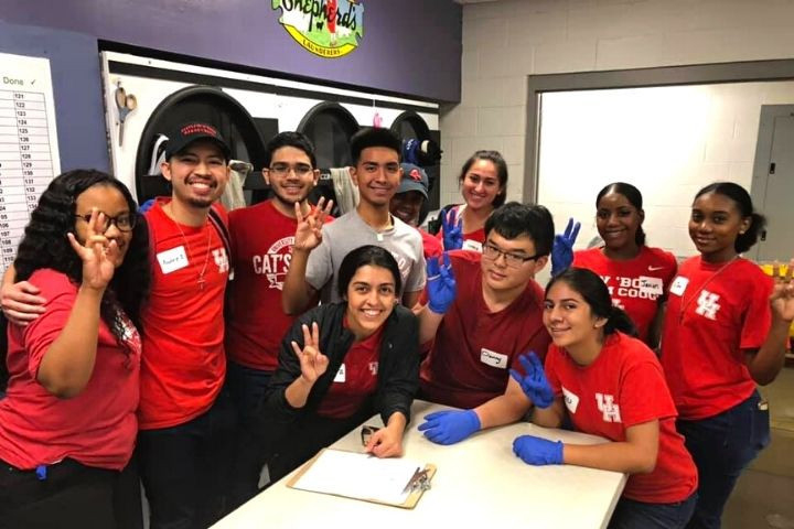 University of Houston students volunteering together at the Metropolitan Volunteer Program, a community service event, smiling and holding up the Cougar hand sign